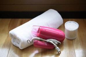 Una toalla blanca, un secador rosa y un recipiente blanco sobre una superficie de madera.