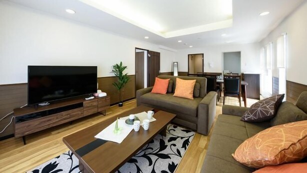 A modern living room with a flat-screen TV, a sofa, a coffee table, and a dining area. - Dynasty 24 (Sapporo)