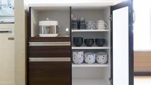 A kitchen with a built-in oven, a microwave, and a coffee maker on the countertop. There are shelves with various kitchenware including bowls and cups. - Dynasty 24 (Sapporo)
