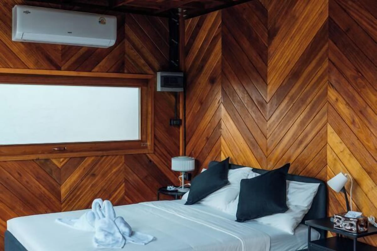 A wooden herringbone wall, a bed with white bedding, a bedside lamp, and a window.