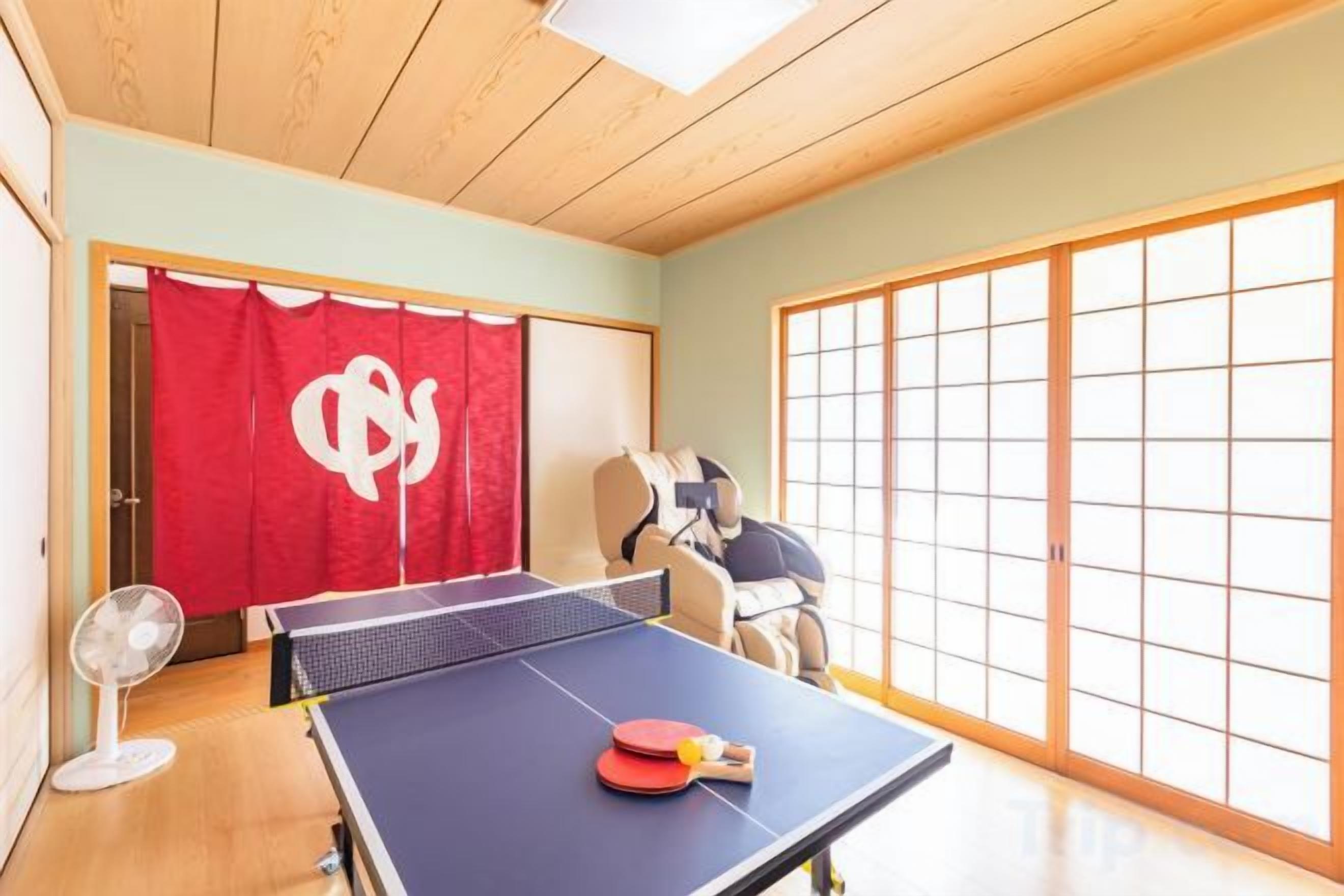 A room with a ping pong table, a fan, and a red curtain with a white symbol.