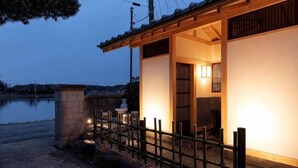 Un edificio japonés tradicional con valla de madera, base de piedra y vista a un cuerpo de agua.