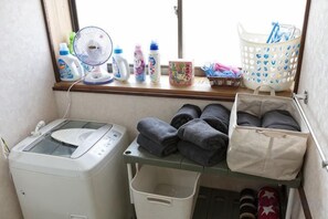 A laundry area with a washing machine, a drying rack, a basket, and a shelf with folded towels. - Tsubakihausu (Kozaki)
