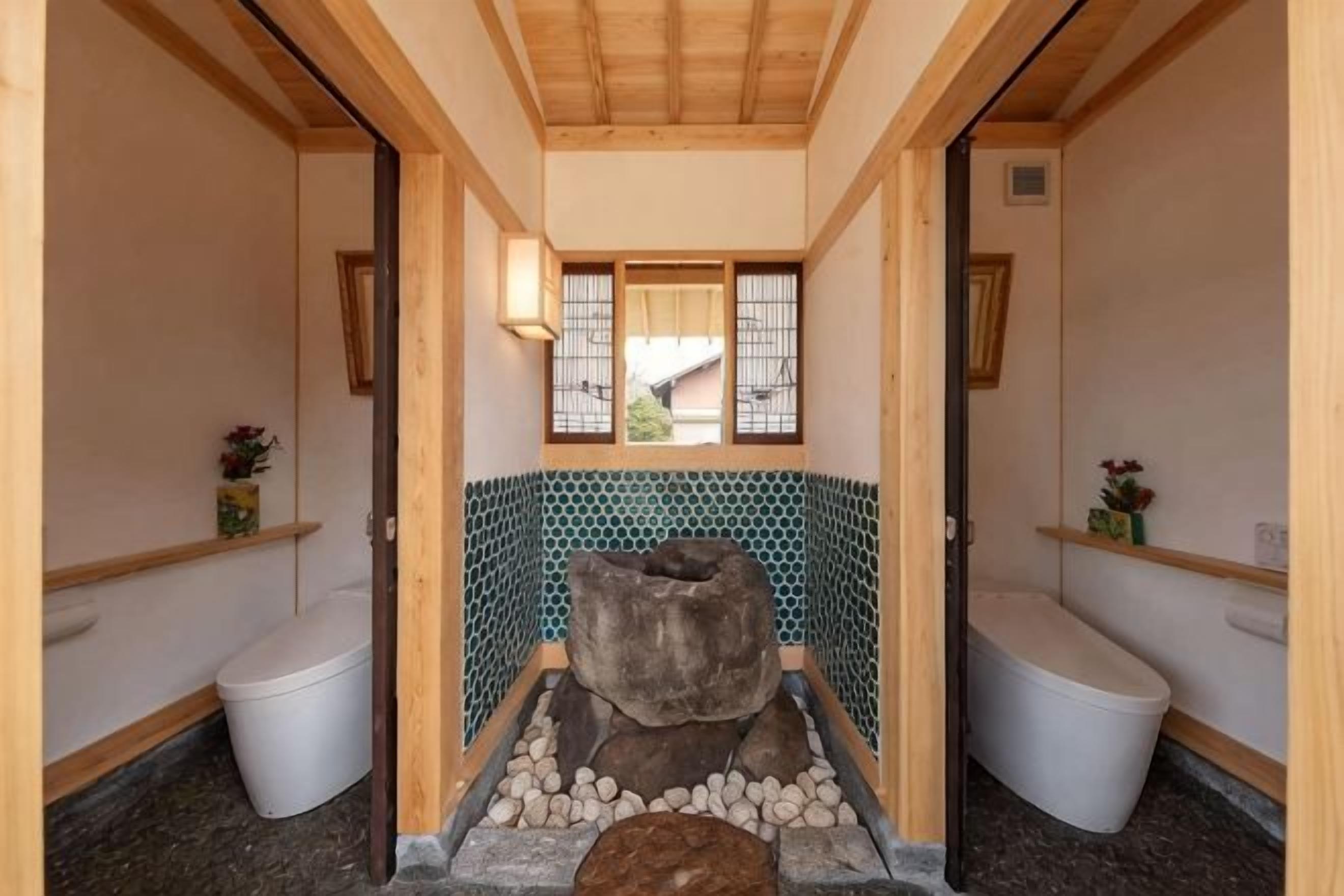 A traditional Japanese-style bathroom with a stone basin, wooden beams, and a tiled wall.