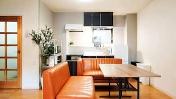 A compact living space with a kitchenette, a dining area with a table and orange seating, and a wooden floor.