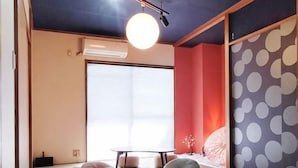 A tatami mat room with a sliding door, a tatami mat table, a low table, and a hanging light fixture. - Aladdin House (Tokyo)