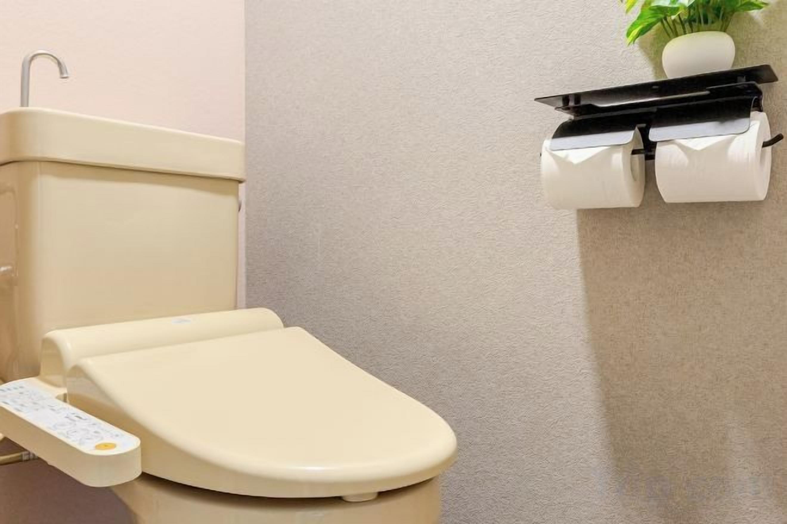 A toilet with a control panel, a toilet paper holder, and a plant on the wall.
