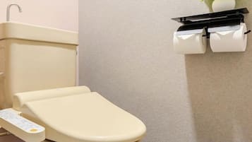 A toilet with a control panel, a toilet paper holder, and a plant on the wall.