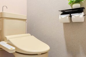Sanitário com painel de controle, rolo de papel higiénico e planta na parede.