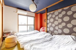 A room with two beds, a window, a wall with a polka dot pattern, and a ceiling light. - Aladdin House (Tokyo)
