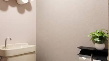 A bathroom with a sink, toilet paper holder, and a potted plant.
