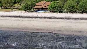 A beach with a building in the background, surrounded by trees. - Tanoma Sumba Beach Resort (Kadumbul)