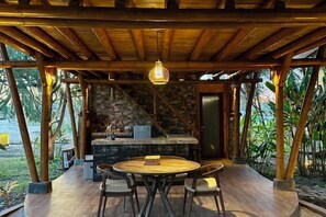 Un espace extérieur abrité, aménagé pour les repas, avec une table ronde et des chaises, un luminaire suspendu et un mur de pierre en arrière-plan.