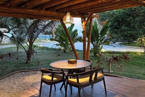 Un espace de restauration en plein air avec une table ronde et des chaises, entouré de plantes tropicales et offrant une vue sur la mer.