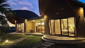 A modern house with a curved roof, large glass windows, and a well-lit interior. - Tanoma Sumba Beach Resort (Kadumbul)
