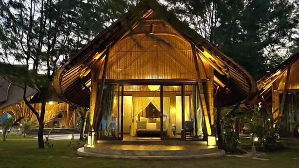 A thatched-roof structure with a glass entrance, a bed, and a small seating area visible inside. - Tanoma Sumba Beach Resort (Kadumbul)