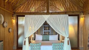 A room with a bed, a bench, a wall-mounted shelf, and a decorative door. - Tanoma Sumba Beach Resort (Kadumbul)