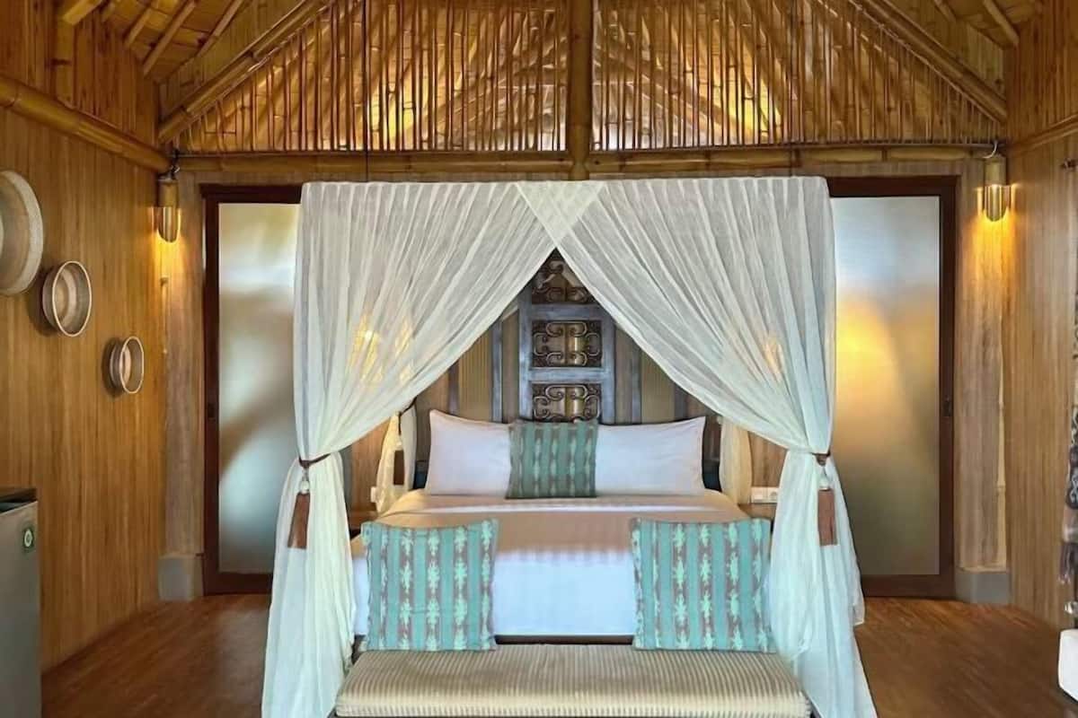 Una habitación con cama, un banco, un estante en la pared y una puerta decorativa.