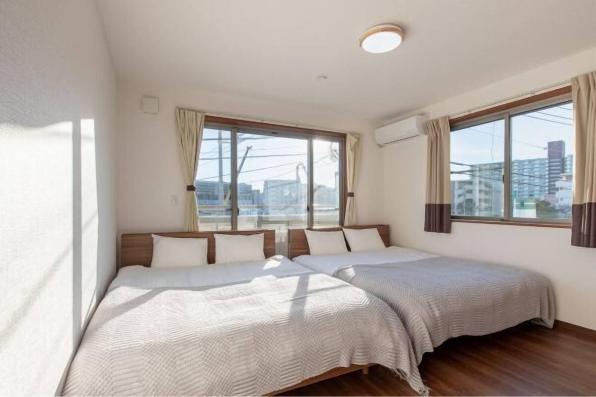 A hotel room with two beds, large windows, and a view of buildings.
