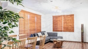 A modern living room with a grey sofa, wooden chairs, a coffee table, and wooden blinds on the windows. - Residential Voyan Minamisunacho (Tokyo)
