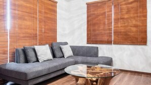 A modern living room with a grey sofa, a glass coffee table, and wooden blinds. - Residential Voyan Minamisunacho (Tokyo)