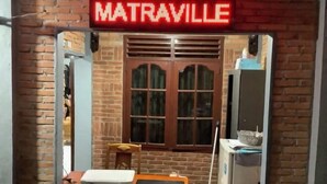 Un edificio de ladrillo con un letrero de neón que dice "MATRAVILLE" sobre una puerta de madera.