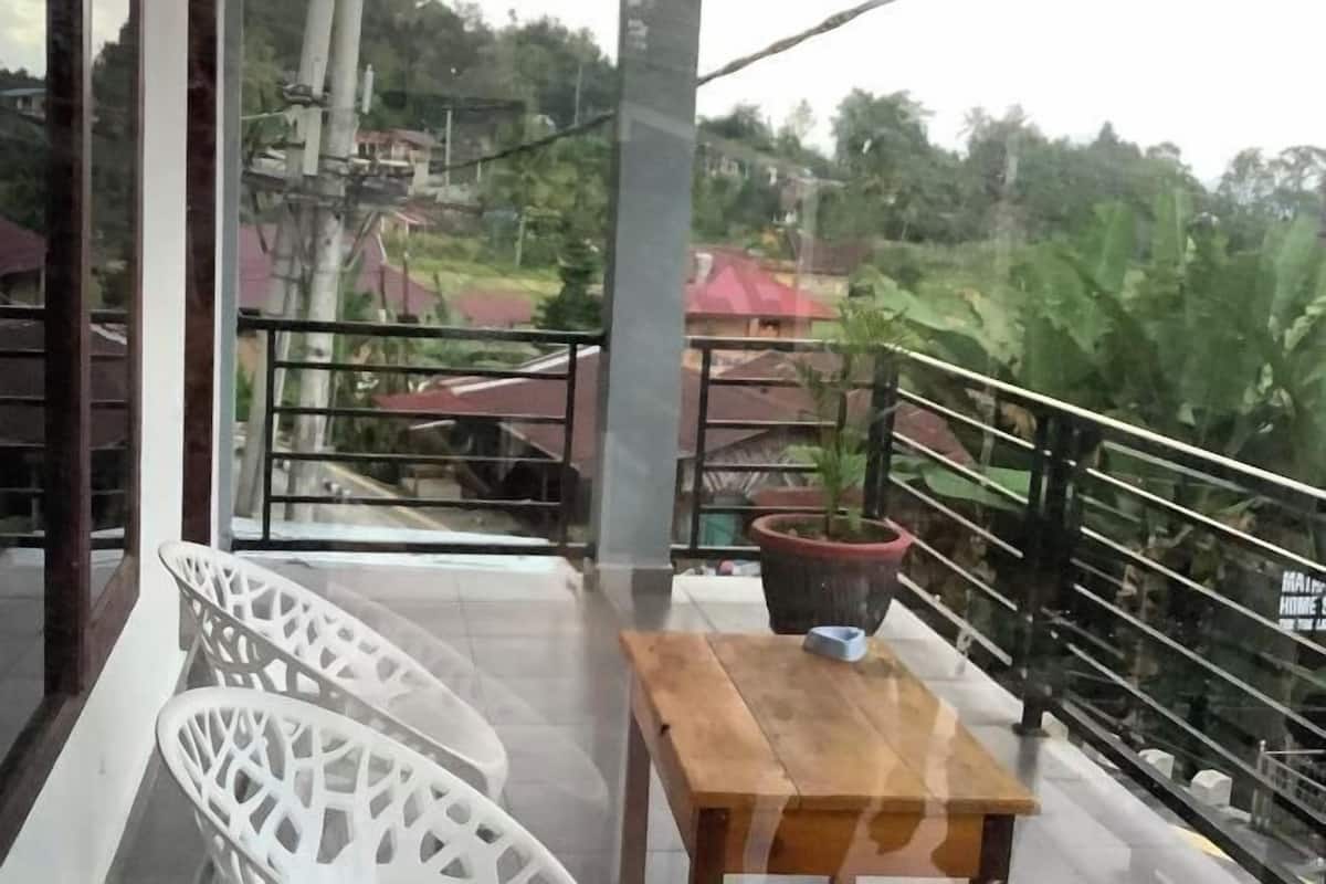 A balcony with a wooden table and chairs, a potted plant, and a view of a residential area with houses and trees.