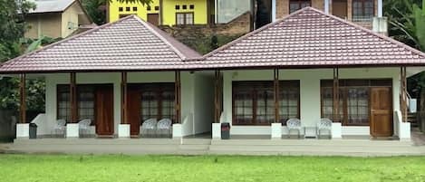 A two-story building with a tiled roof, a porch with seating, and a grassy lawn.