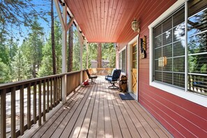 A wooden deck with a red building, two chairs, and a small table. - Dogwood Star – Star Location + Cozy Vibes (Shaver Lake)