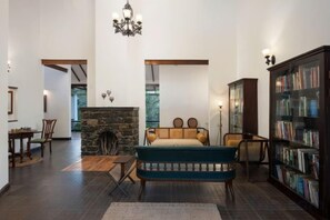 A spacious living room with a stone fireplace, a large bookshelf, and a comfortable seating area. - Reen Resorts Aanavilasam Plantation Thekkady (Thekkady)