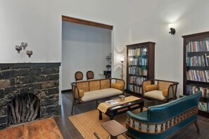Een woonkamer met een open haard, een bank, een salontafel en een boekenplank.