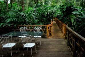 A wooden deck with a table and chairs, surrounded by dense foliage. - Reen Resorts Aanavilasam Plantation Thekkady (Thekkady)