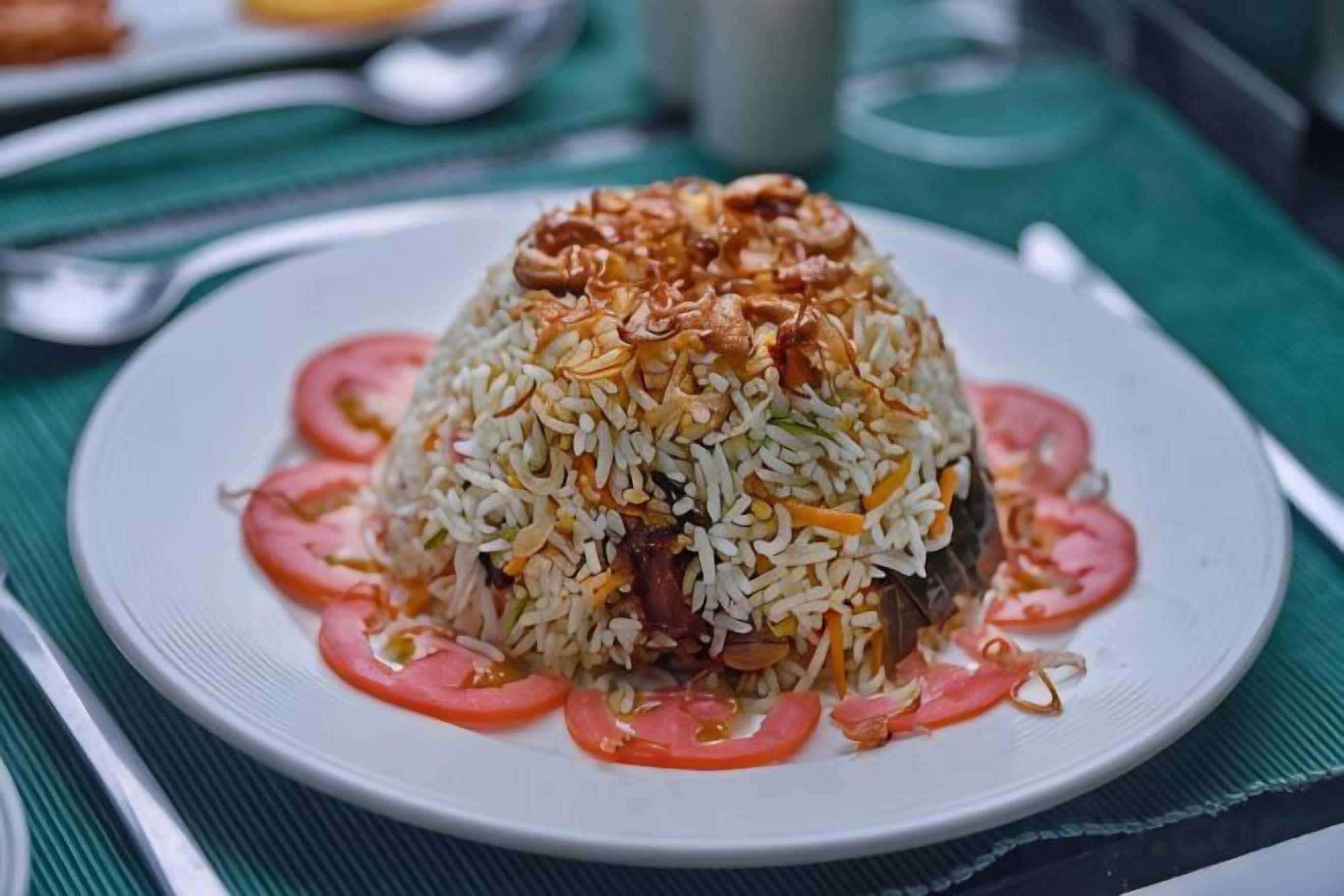 A plate of rice with meat and tomatoes on a white plate.