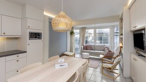 A modern kitchen with white cabinetry, a microwave, and a hanging woven light fixture. - Cosy Studio With Seaview Wenduine - L'ancre (De Haan)