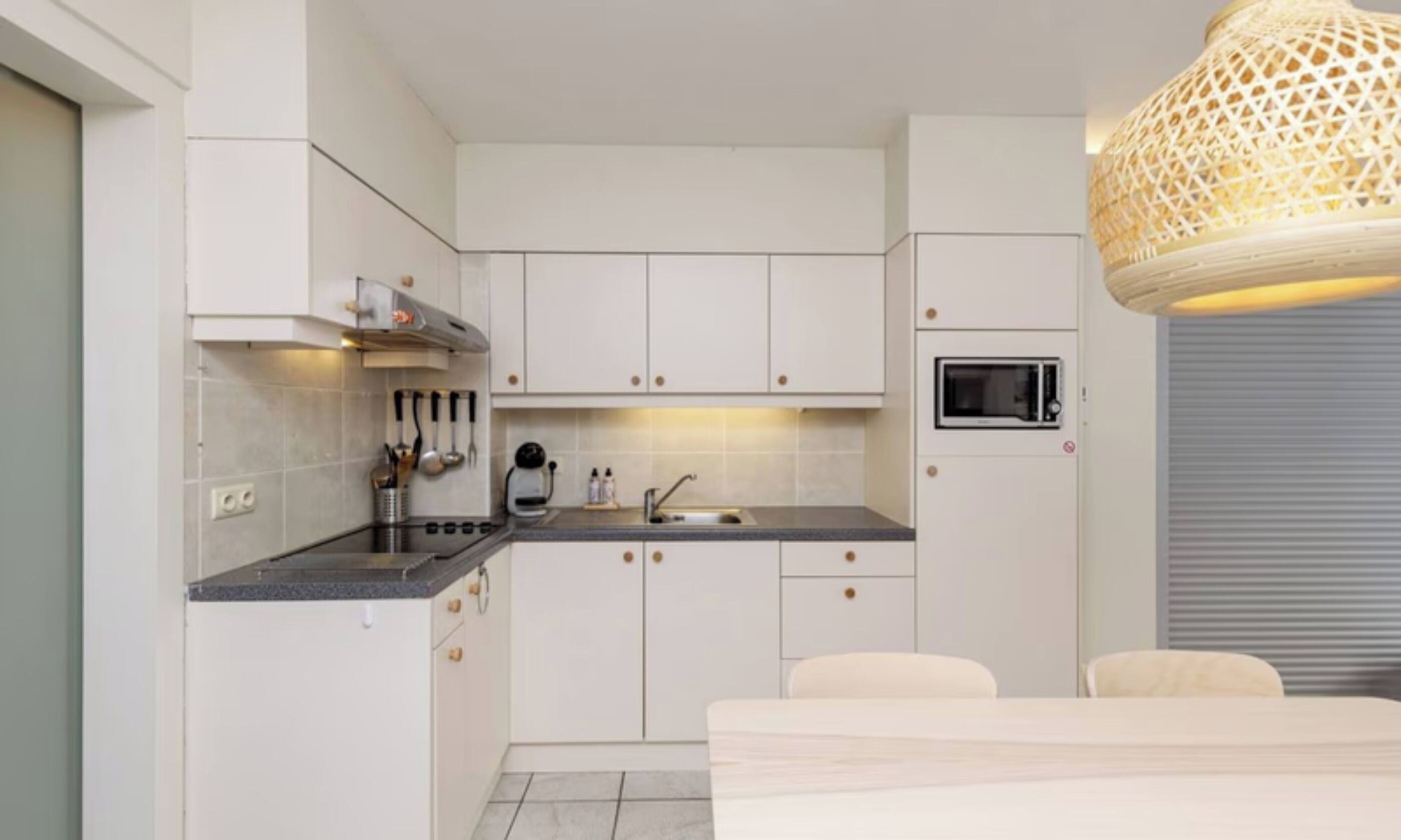 A compact kitchen with white cabinets, a built-in microwave, and a hanging light fixture.