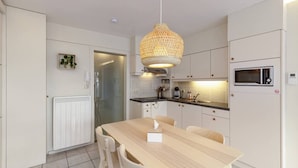 A modern kitchen with white cabinetry, a wooden dining table, and a hanging light fixture. - Cosy Studio With Seaview Wenduine - L'ancre (De Haan)
