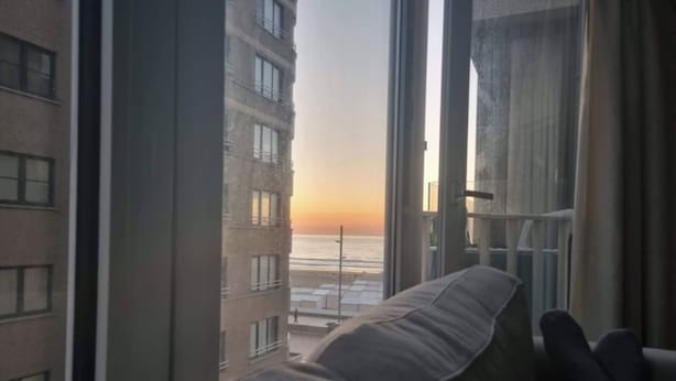 A room with a view of the beach at sunset, a bed, and a window with curtains. - Cosy Studio With Seaview Wenduine - L'ancre (De Haan)