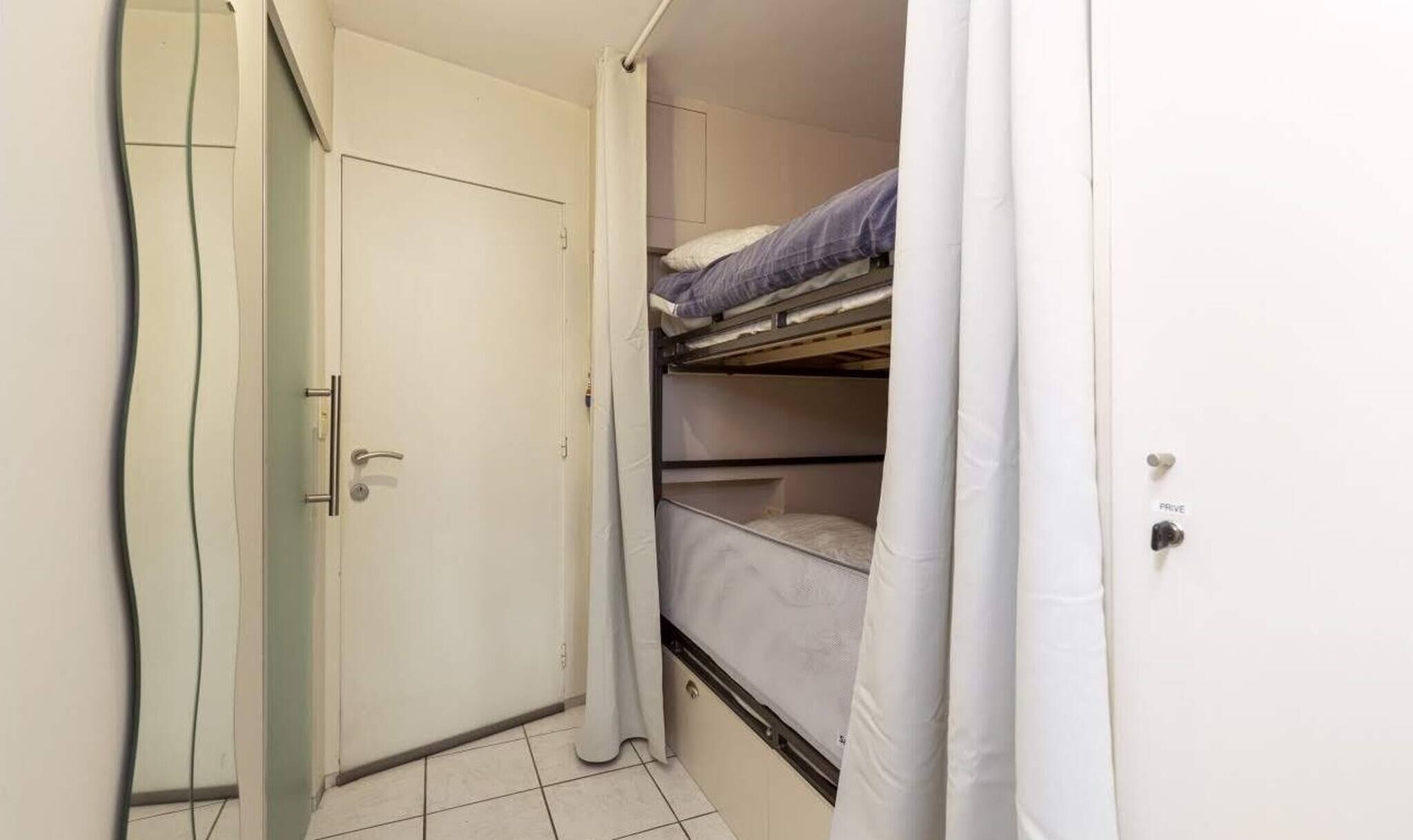 A small, compact room with a bunk bed, a door, and a curtain.