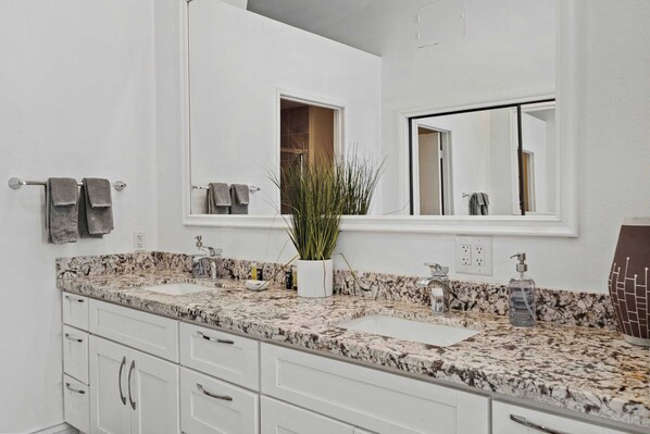 A modern bathroom with a marble countertop, white cabinetry, a large mirror, and a potted plant. - The Preserve at Mesquite For 4 (Palm Springs)