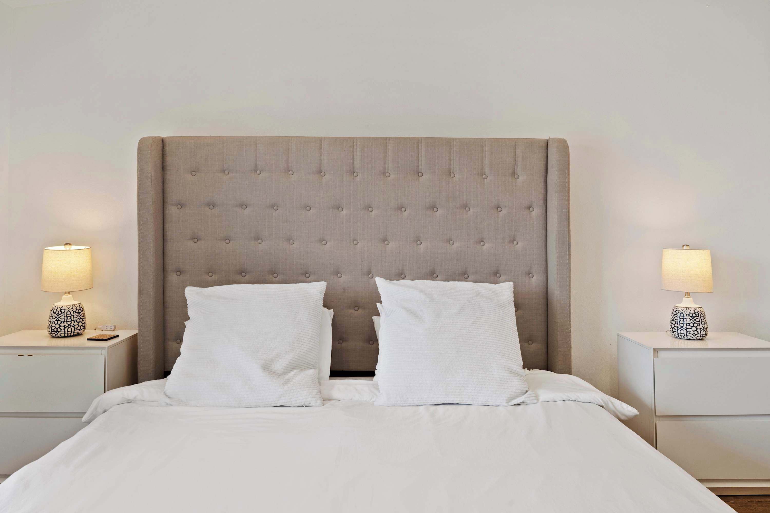 A neatly made bed with a tufted headboard, white bedding, and two bedside tables with lamps.