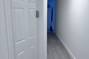 A hallway with a white door, a blue wall, and a floor with a light-colored wood finish. - Modern Garden Retreat - Near Wfj, 3Br Ensuite & Parking (Watford)