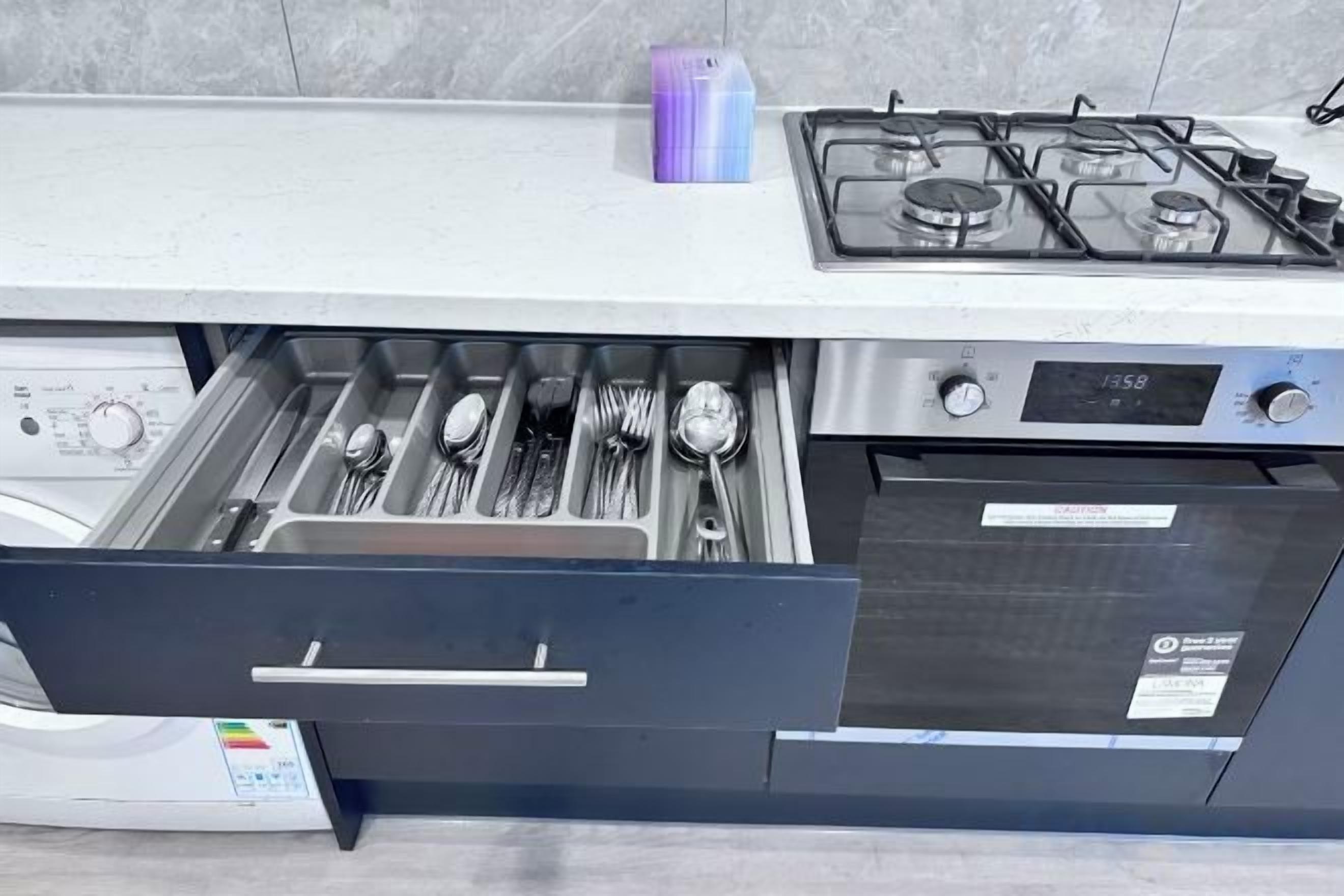 A kitchen with a built-in dishwasher, a gas stove, and a drawer with utensils.