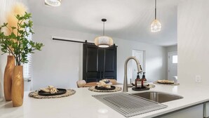 A modern kitchen with a white countertop, stainless steel sink, and pendant lighting.