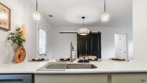 A modern kitchen with a large island, stainless steel appliances, pendant lighting, and a view of the living area.
