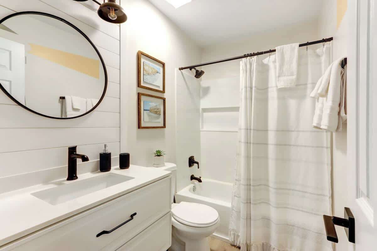 A modern bathroom with a white vanity, a round mirror, a bathtub, and a shower curtain.