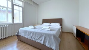 A neatly made bed with white linens and folded towels, a wooden floor, a radiator, and a window with a view of a brick wall. - Time Traveller's Mansion in Fatih (Istanbul)