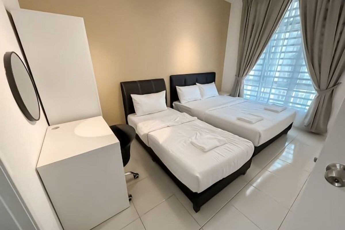A hotel room with two beds, a bedside table, a mirror, and a window with curtains.