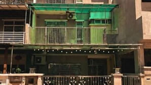 A multi-story residential building with balconies, a green awning, and a decorative fence.