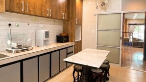A kitchen with wooden cabinets, a marble countertop, a coffee machine, and a dining area with stools.
