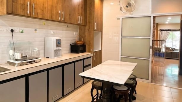 Una cocina con armarios de madera, encimera de mármol, cafetera y una zona de comedor con taburetes.